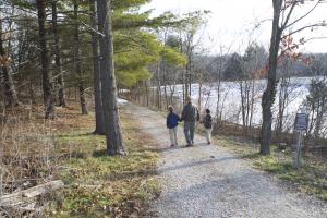 A man in a hat walks with boys along a gravel path next to a body of water.