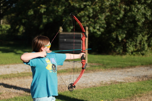 Little girl draws back arrow on her bow