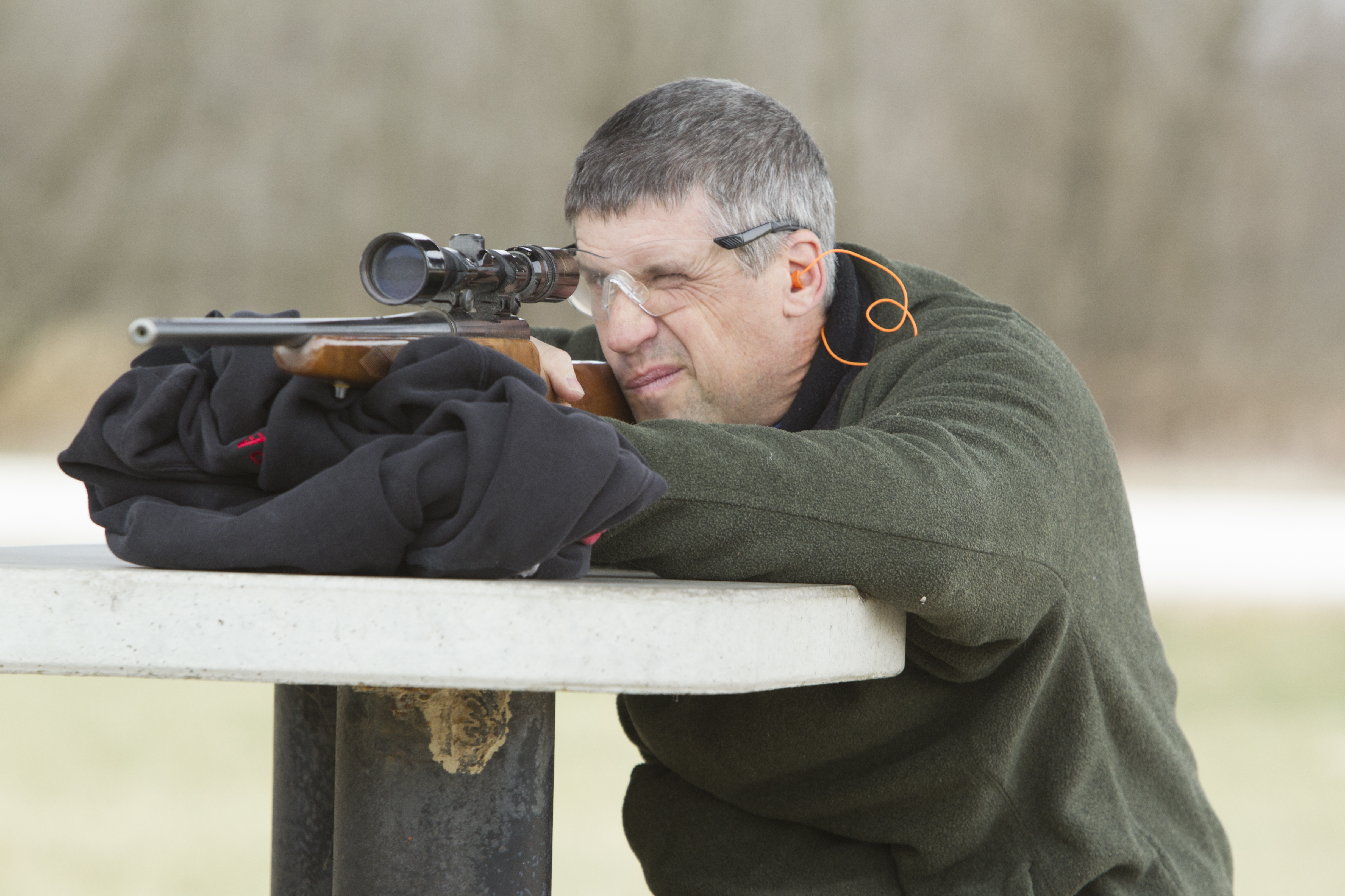 A man looks through a sight on his rifle at a shooting range.